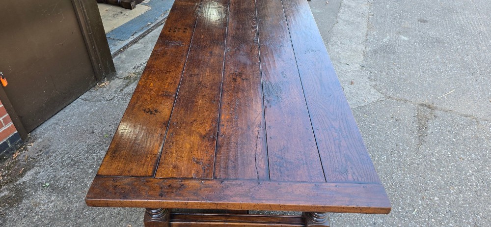 A large solid oak refectory dining table featuring a wide plank top, breadboard ends, turned baluster legs, and a low H-stretcher base. View VI