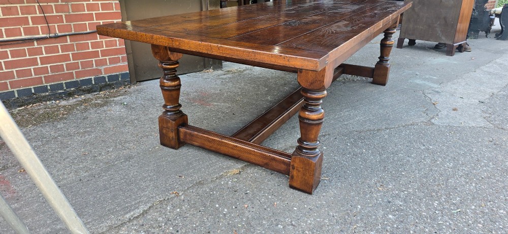 A large solid oak refectory dining table featuring a wide plank top, breadboard ends, turned baluster legs, and a low H-stretcher base. View VIII