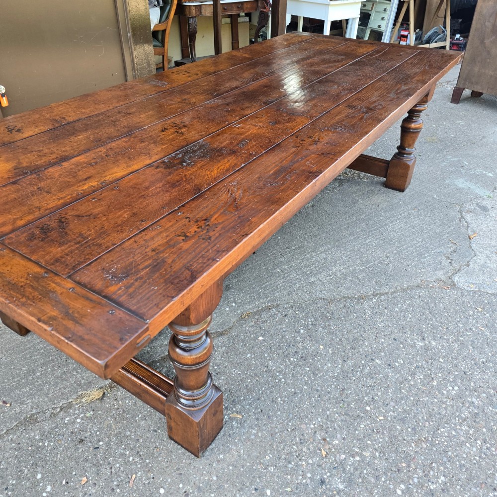 A large solid oak refectory dining table featuring a wide plank top, breadboard ends, turned baluster legs, and a low H-stretcher base. View X