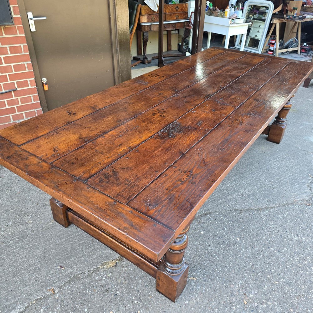 A large solid oak refectory dining table featuring a wide plank top, breadboard ends, turned baluster legs, and a low H-stretcher base. View XI