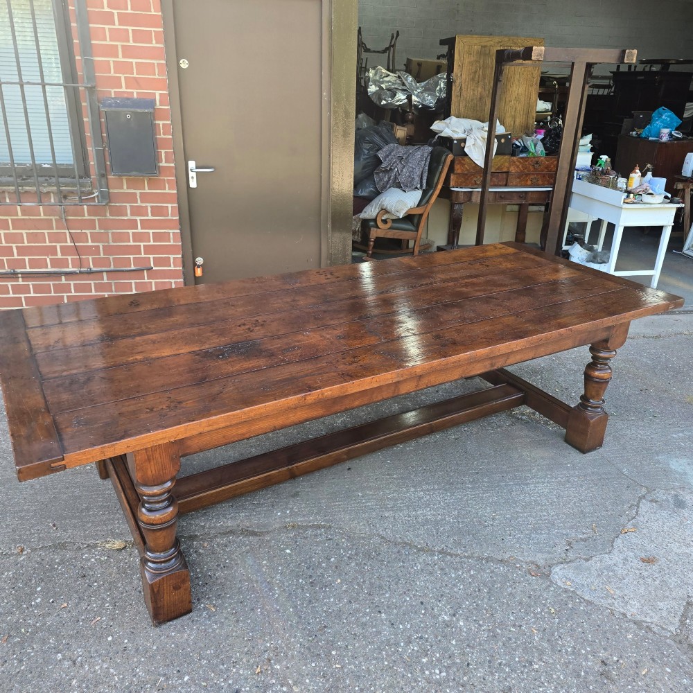 A large solid oak refectory dining table featuring a wide plank top, breadboard ends, turned baluster legs, and a low H-stretcher base. View XII