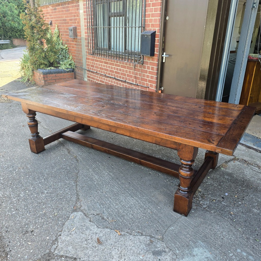 A large solid oak refectory dining table featuring a wide plank top, breadboard ends, turned baluster legs, and a low H-stretcher base. View XIII