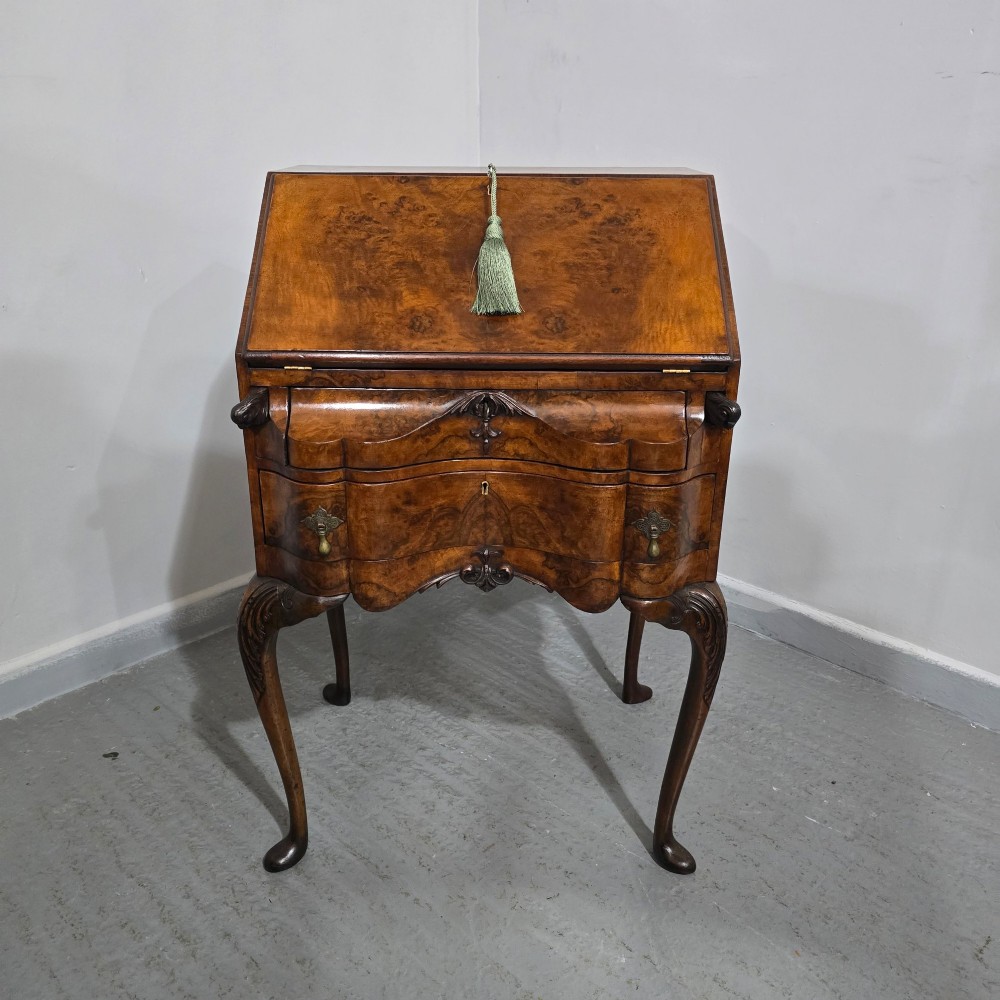 A Queen Anne style burr walnut writing bureau featuring a sloped front lid, shaped drawers with brass drop handles, and tall cabriole legs. View VI