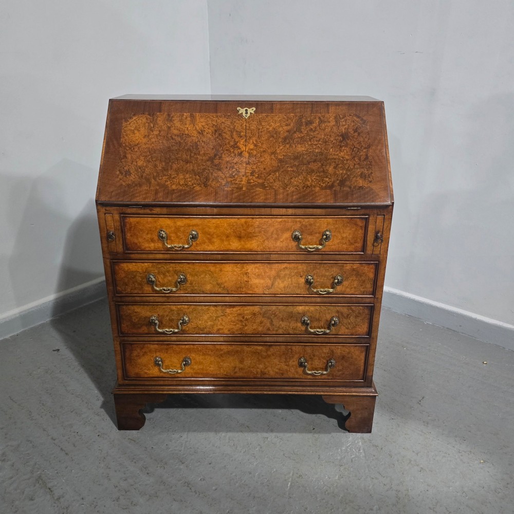 An antique Queen Anne burr walnut writing bureau featuring a sloping fall-front lid over four graduated drawers with brass drop handles and bracket feet. View II