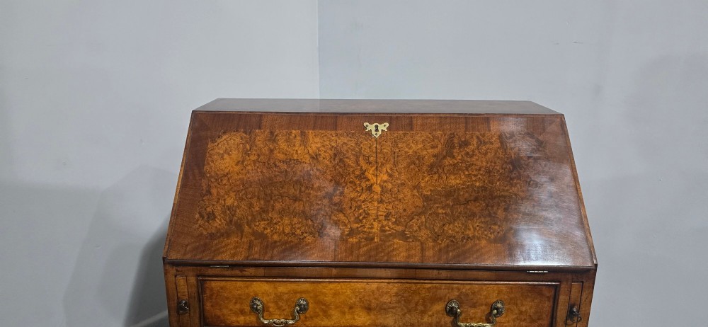An antique Queen Anne burr walnut writing bureau featuring a sloping fall-front lid over four graduated drawers with brass drop handles and bracket feet. View V