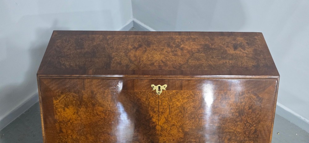 An antique Queen Anne burr walnut writing bureau featuring a sloping fall-front lid over four graduated drawers with brass drop handles and bracket feet. View VI