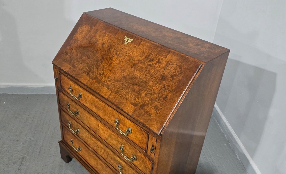 An antique Queen Anne burr walnut writing bureau featuring a sloping fall-front lid over four graduated drawers with brass drop handles and bracket feet. View VIII