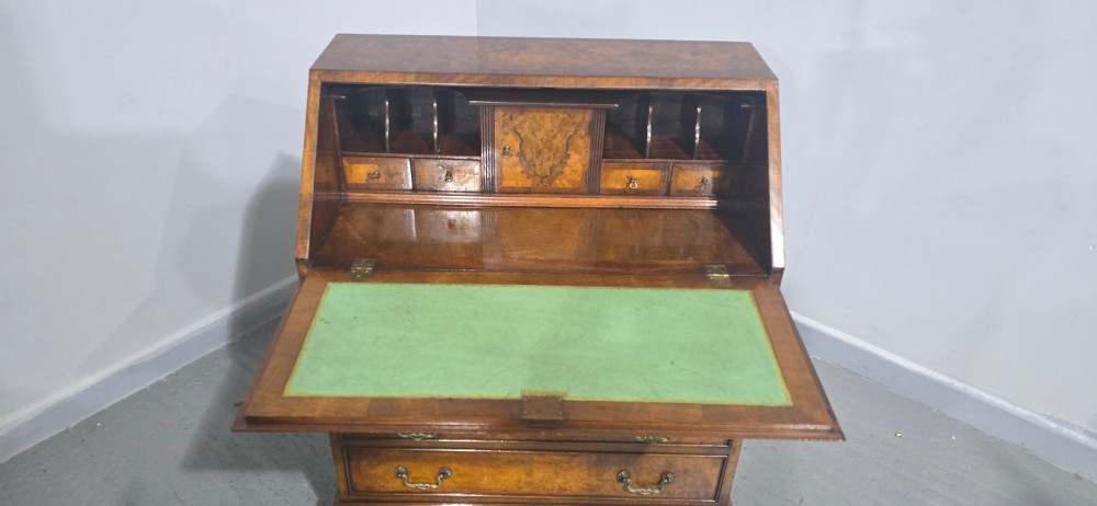 An antique Queen Anne burr walnut writing bureau featuring a sloping fall-front lid over four graduated drawers with brass drop handles and bracket feet. View XI