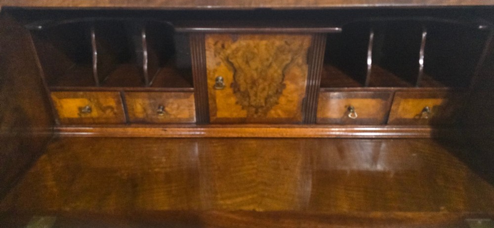 An antique Queen Anne burr walnut writing bureau featuring a sloping fall-front lid over four graduated drawers with brass drop handles and bracket feet. View XII