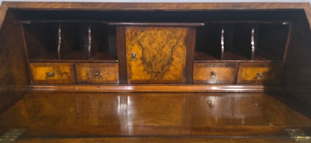 An antique Queen Anne burr walnut writing bureau featuring a sloping fall-front lid over four graduated drawers with brass drop handles and bracket feet. View XIII