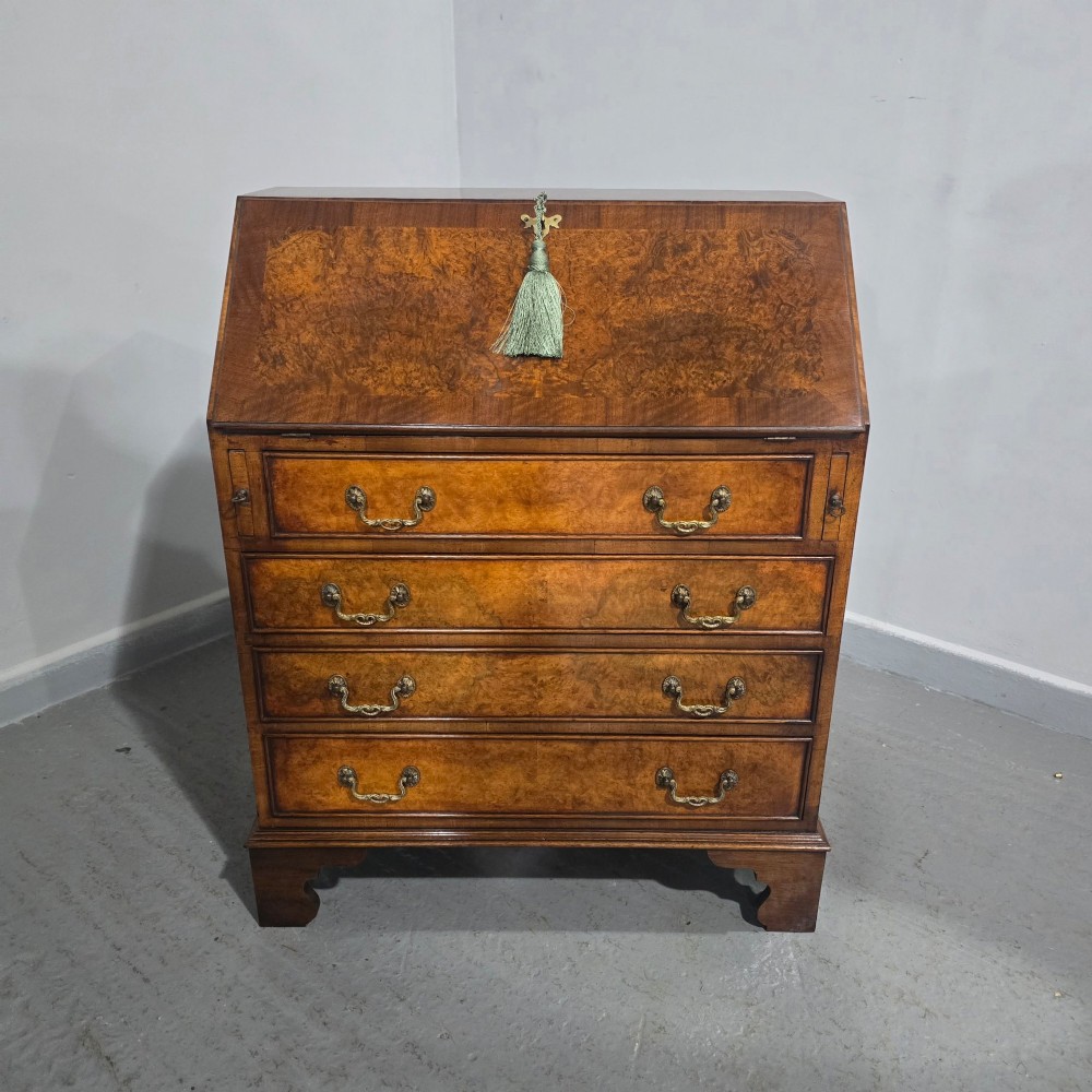 An antique Queen Anne burr walnut writing bureau featuring a sloping fall-front lid over four graduated drawers with brass drop handles and bracket feet. View XV