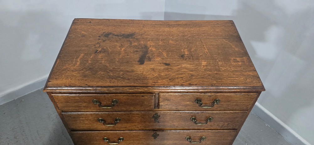 A Georgian oak chest of drawers featuring two short drawers above three long graduated drawers with brass swan-neck handles and bracket feet. View VI