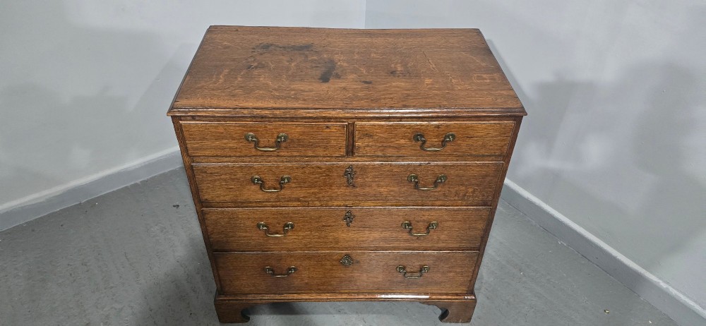 A Georgian oak chest of drawers featuring two short drawers above three long graduated drawers with brass swan-neck handles and bracket feet. View VII