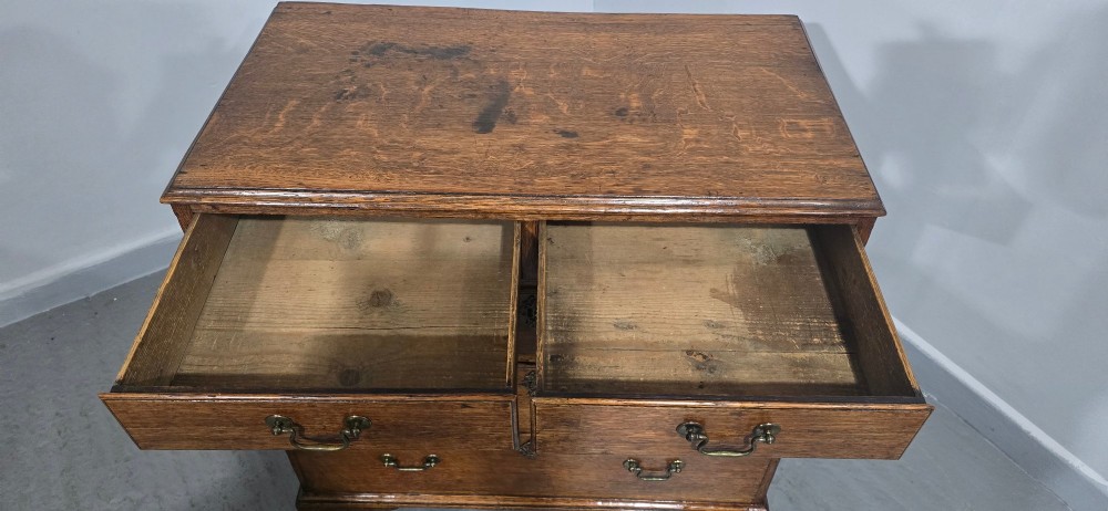 A Georgian oak chest of drawers featuring two short drawers above three long graduated drawers with brass swan-neck handles and bracket feet. View IX