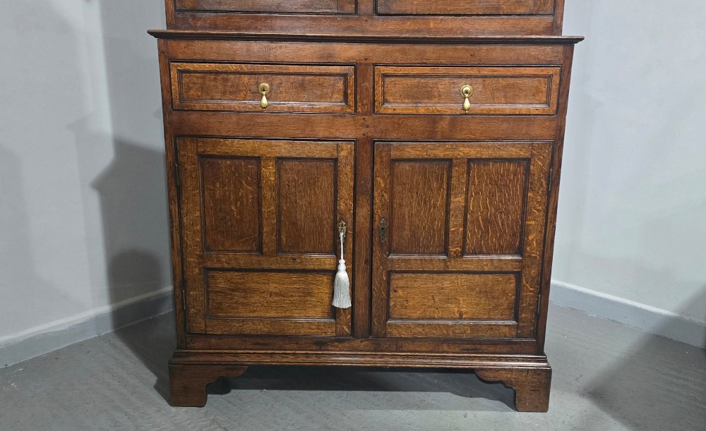 A dark oak Georgian court cupboard featuring an upper cabinet with arched panel doors, two central drawers, and a lower double-door cupboard on bracket feet. View II