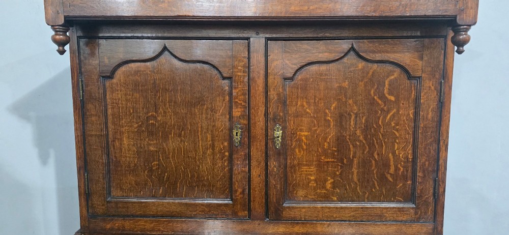 A dark oak Georgian court cupboard featuring an upper cabinet with arched panel doors, two central drawers, and a lower double-door cupboard on bracket feet. View VI