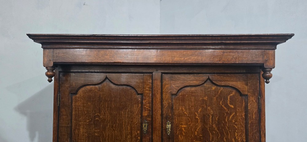A dark oak Georgian court cupboard featuring an upper cabinet with arched panel doors, two central drawers, and a lower double-door cupboard on bracket feet. View VII