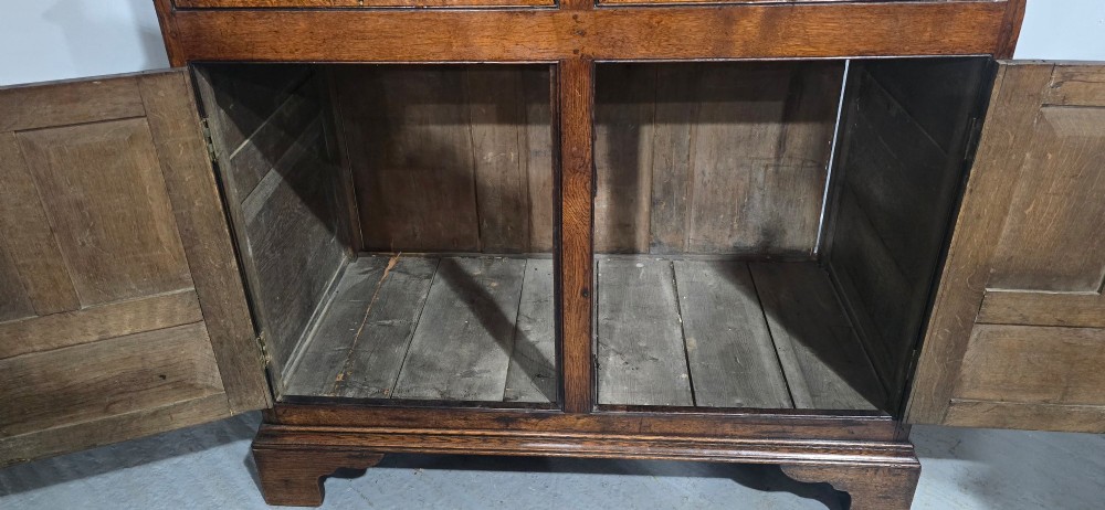 A dark oak Georgian court cupboard featuring an upper cabinet with arched panel doors, two central drawers, and a lower double-door cupboard on bracket feet. View XIV