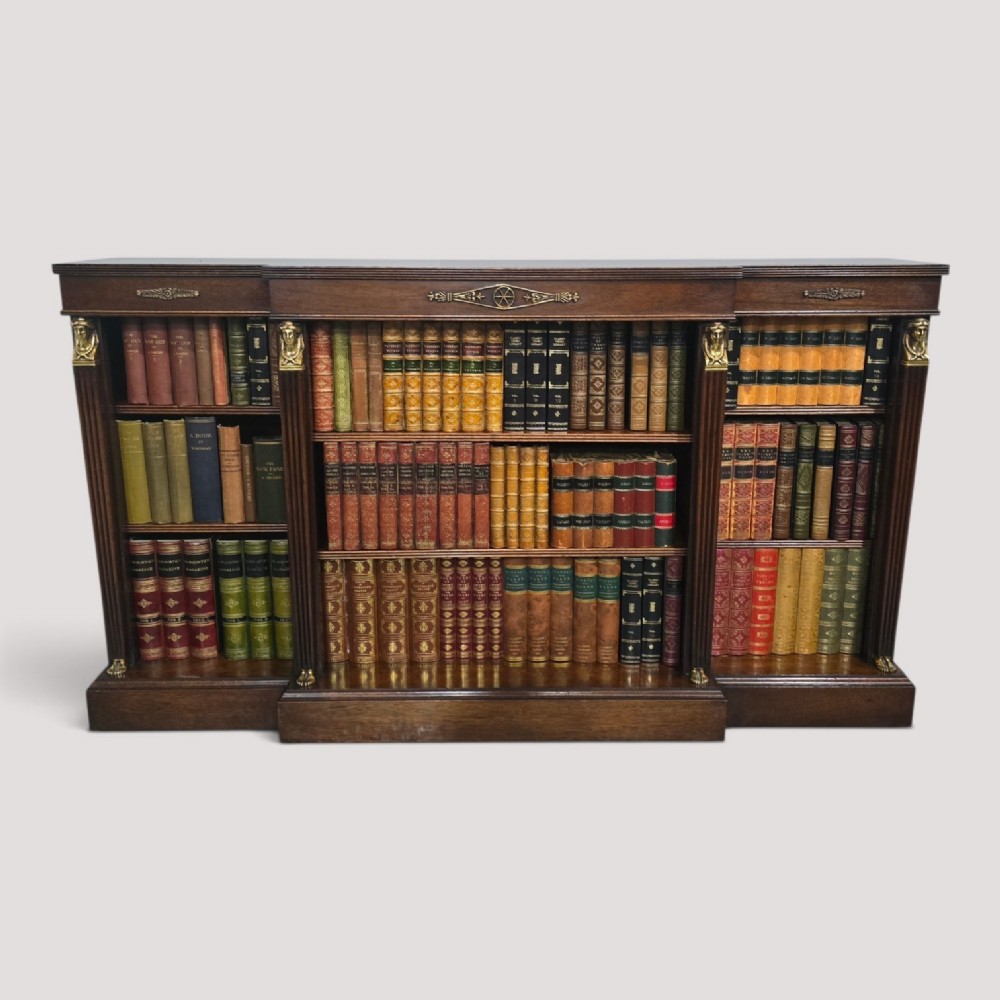 An antique Empire style breakfront low mahogany bookcase featuring three sections of open adjustable shelves filled with books and adorned with gilt bronze mounts and fluted pilasters.