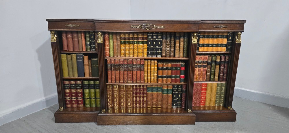 An antique Empire style breakfront low mahogany bookcase featuring three sections of open adjustable shelves filled with books and adorned with gilt bronze mounts and fluted pilasters. View II