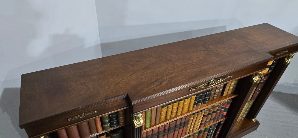 An antique Empire style breakfront low mahogany bookcase featuring three sections of open adjustable shelves filled with books and adorned with gilt bronze mounts and fluted pilasters. View XV
