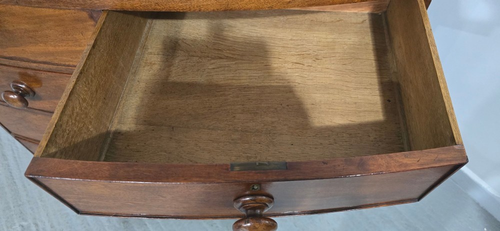 An antique mahogany bow-front chest of drawers featuring two short drawers over three long graduated drawers with turned wooden knobs. View VII