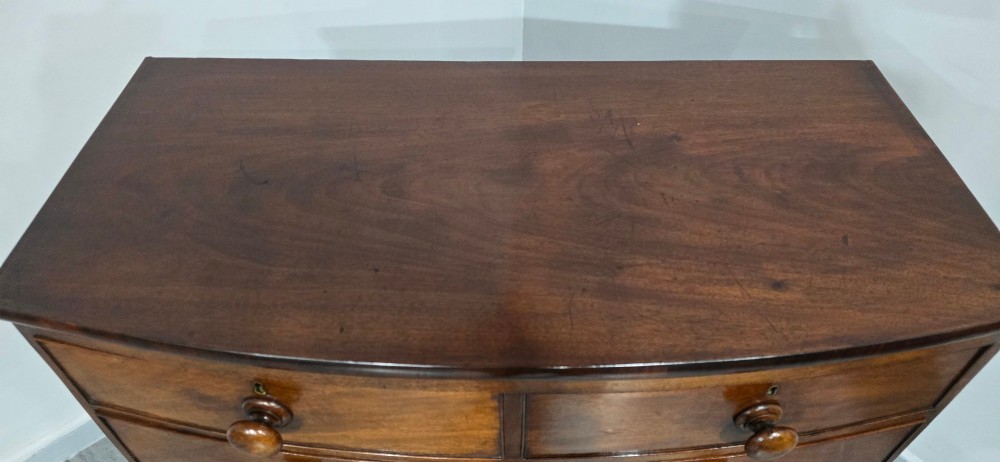 An antique mahogany bow-front chest of drawers featuring two short drawers over three long graduated drawers with turned wooden knobs. View VIII