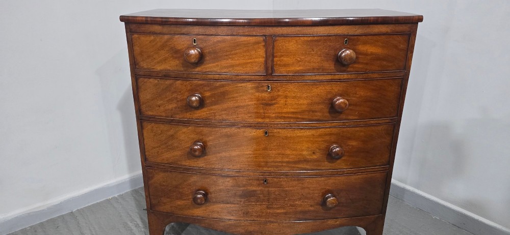 An antique mahogany bow-front chest of drawers featuring two short drawers over three long graduated drawers with turned wooden knobs. View IX