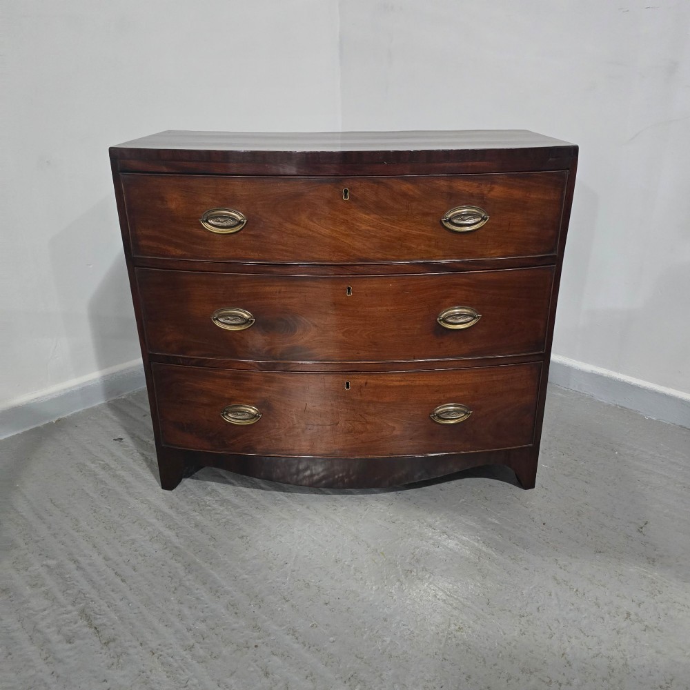 An antique Georgian mahogany bowfront chest featuring three drawers with oval brass handles and keyholes. View II