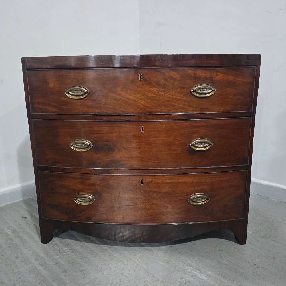 An antique Georgian mahogany bowfront chest featuring three drawers with oval brass handles and keyholes. View III