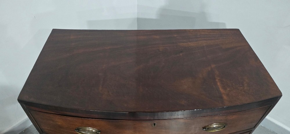 An antique Georgian mahogany bowfront chest featuring three drawers with oval brass handles and keyholes. View VII