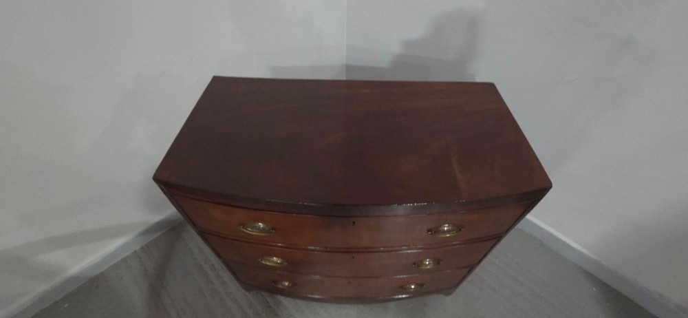 An antique Georgian mahogany bowfront chest featuring three drawers with oval brass handles and keyholes. View XI