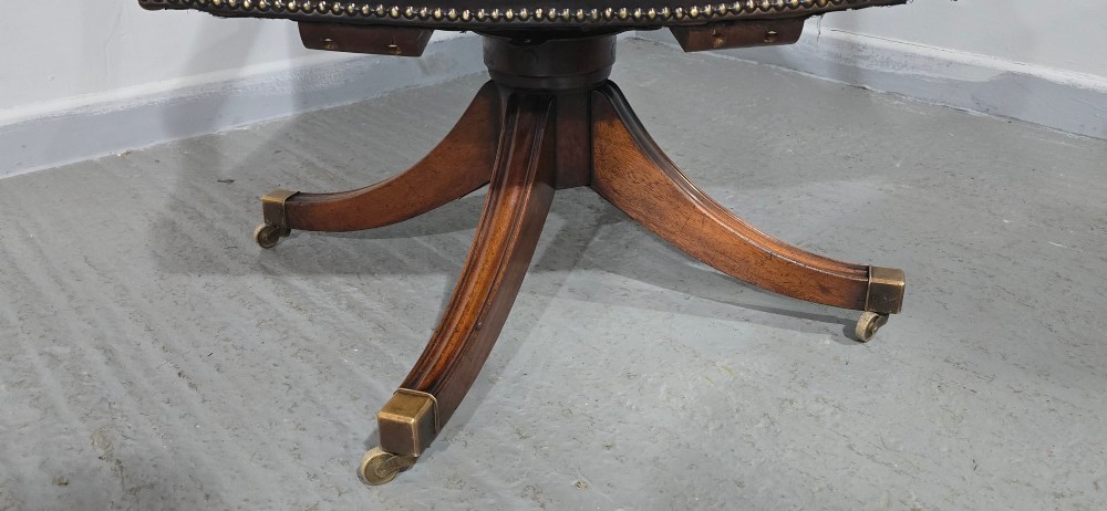 A dark brown leather upholstered swivel desk chair featuring carved mahogany armrests, brass studding, and splayed legs with brass castors. View VII