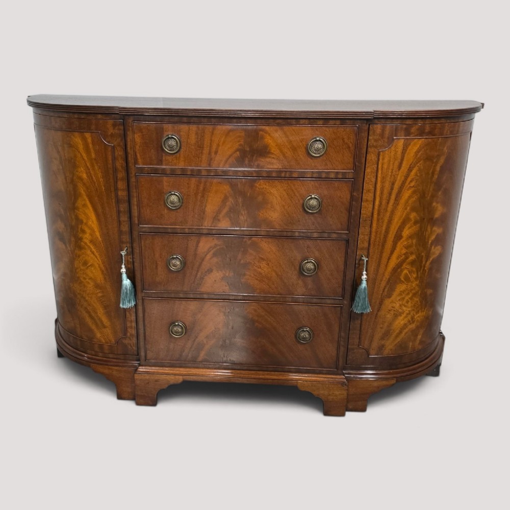 A mahogany bowfront sideboard featuring four central drawers flanked by two curved outer cupboard doors with flame mahogany veneer panels and brass ring handles.