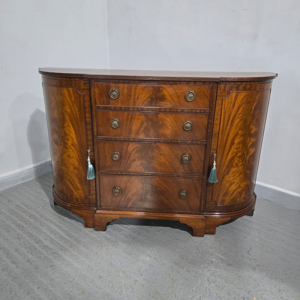 A mahogany bowfront sideboard featuring four central drawers flanked by two curved outer cupboard doors with flame mahogany veneer panels and brass ring handles. View II