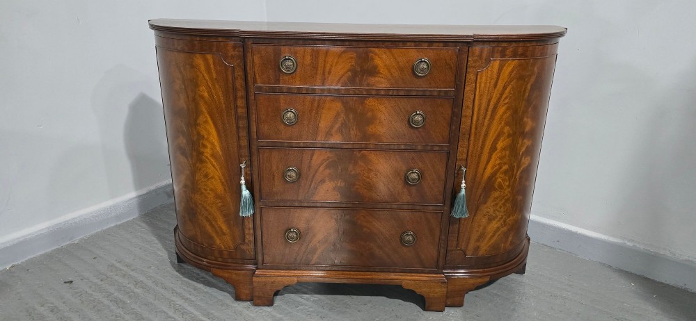 A mahogany bowfront sideboard featuring four central drawers flanked by two curved outer cupboard doors with flame mahogany veneer panels and brass ring handles. View III