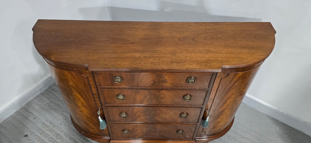 A mahogany bowfront sideboard featuring four central drawers flanked by two curved outer cupboard doors with flame mahogany veneer panels and brass ring handles. View IV