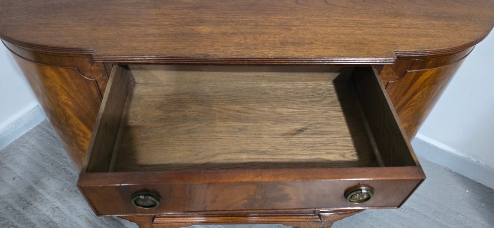 A mahogany bowfront sideboard featuring four central drawers flanked by two curved outer cupboard doors with flame mahogany veneer panels and brass ring handles. View V