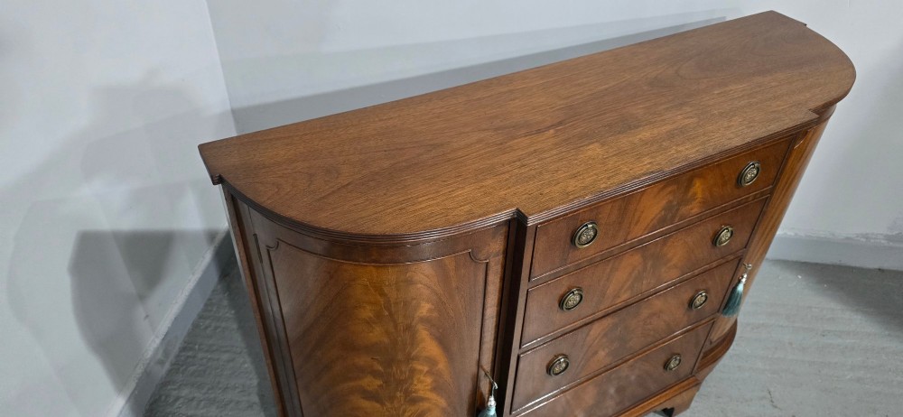 A mahogany bowfront sideboard featuring four central drawers flanked by two curved outer cupboard doors with flame mahogany veneer panels and brass ring handles. View XII