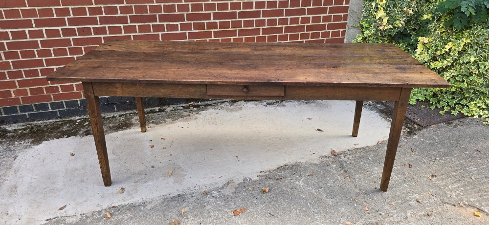 An antique rustic French wooden refectory dining table featuring a three-plank top, single side drawer, and square tapered legs. View III