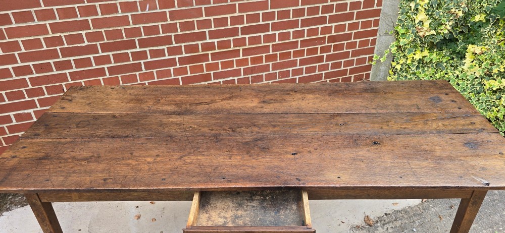An antique rustic French wooden refectory dining table featuring a three-plank top, single side drawer, and square tapered legs. View XII