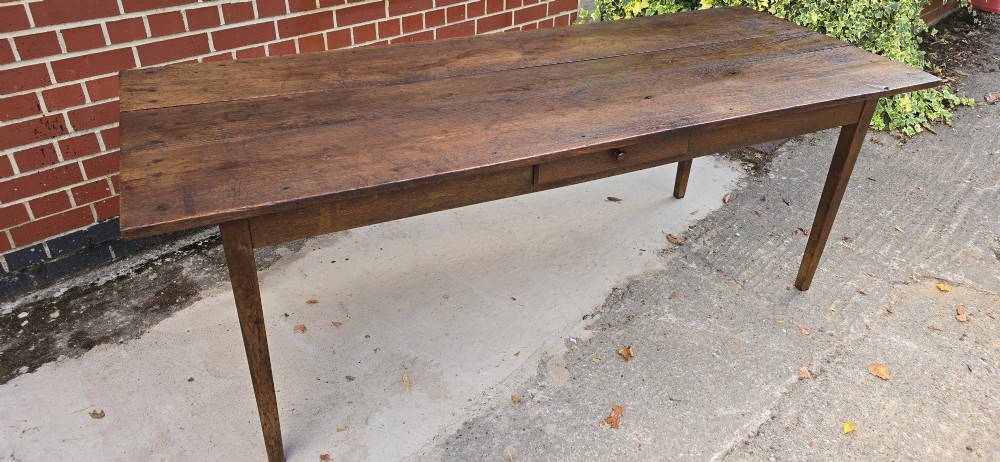 An antique rustic French wooden refectory dining table featuring a three-plank top, single side drawer, and square tapered legs. View XV