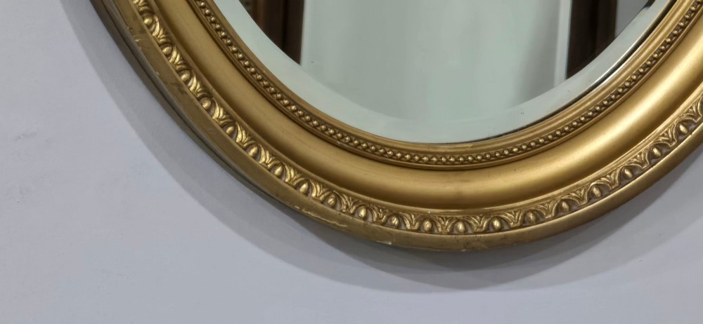 An antique oval wall mirror featuring a gilded frame decorated with beaded and egg-and-dart moulded trim. View V