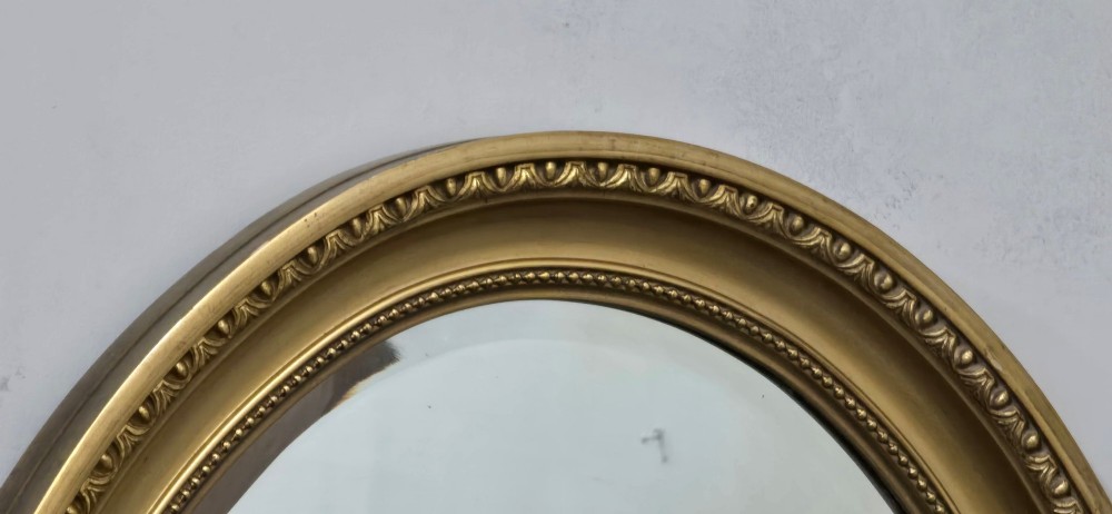 An antique oval wall mirror featuring a gilded frame decorated with beaded and egg-and-dart moulded trim. View VII
