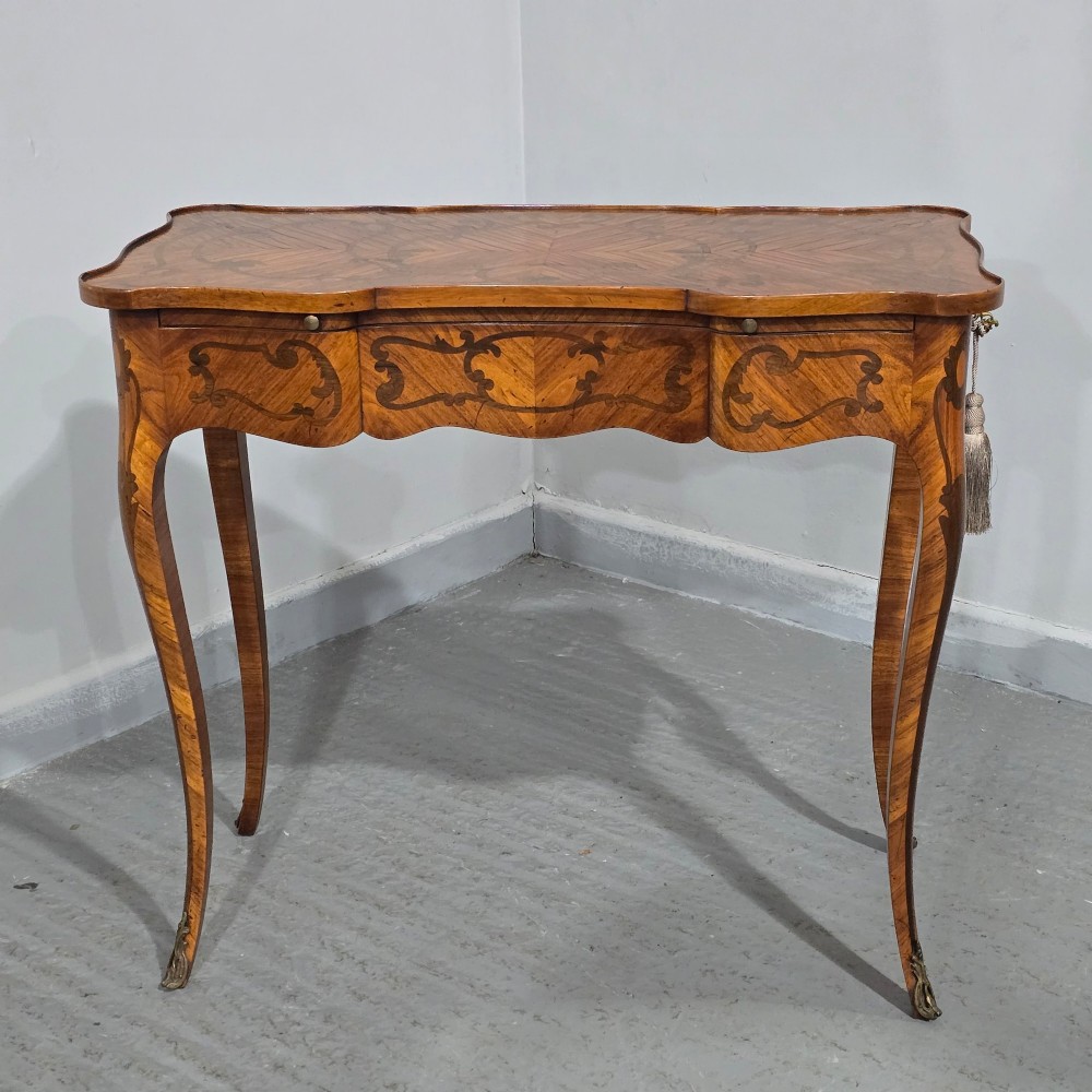 A small French Louis XV style writing table crafted from warm brown wood with scrolling marquetry, a serpentine edge, and slim cabriole legs. View II