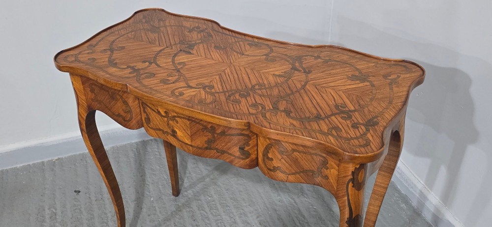 A small French Louis XV style writing table crafted from warm brown wood with scrolling marquetry, a serpentine edge, and slim cabriole legs. View XIV