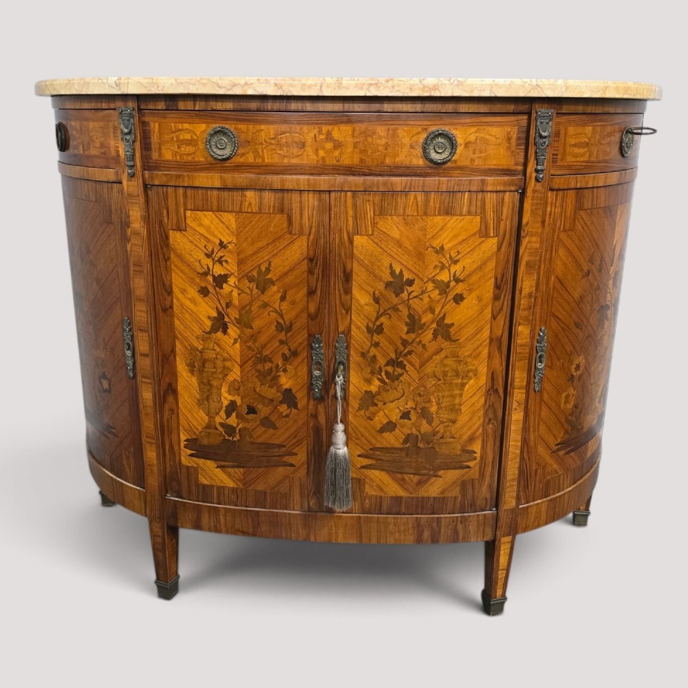 A French Louis XVI style demi-lune cabinet featuring intricate floral marquetry inlay, gilt-bronze mounts, and a contoured marble top.