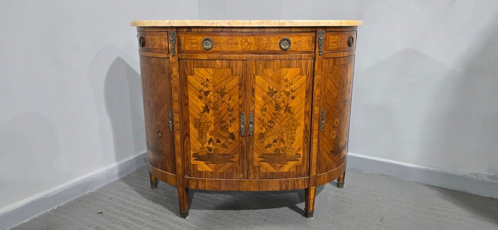 A French Louis XVI style demi-lune cabinet featuring intricate floral marquetry inlay, gilt-bronze mounts, and a contoured marble top. View IV