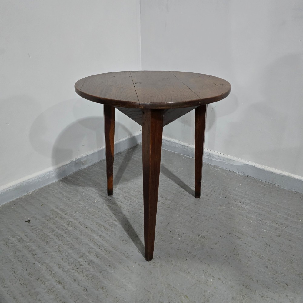 A dark brown Georgian oak cricket table featuring a circular planked top supported by three splayed tapered legs. View II