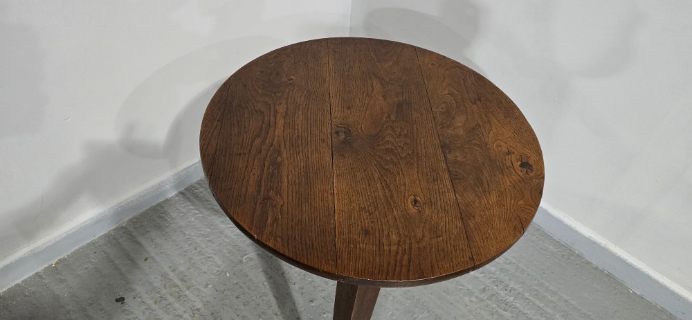 A dark brown Georgian oak cricket table featuring a circular planked top supported by three splayed tapered legs. View IV